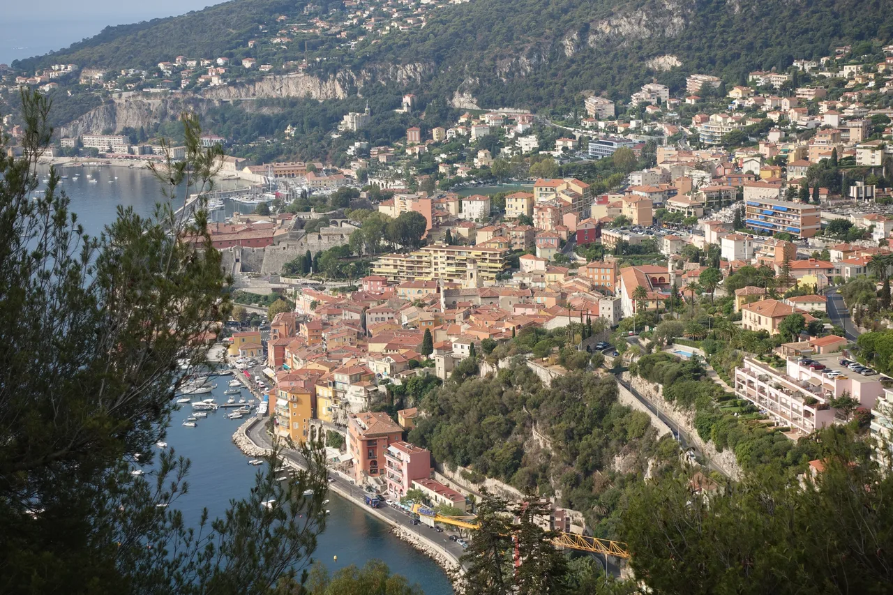 Vue aérienne de la rade de Villefranche-sur-Mer, citadelle, façades colorées du port et collines boisées.