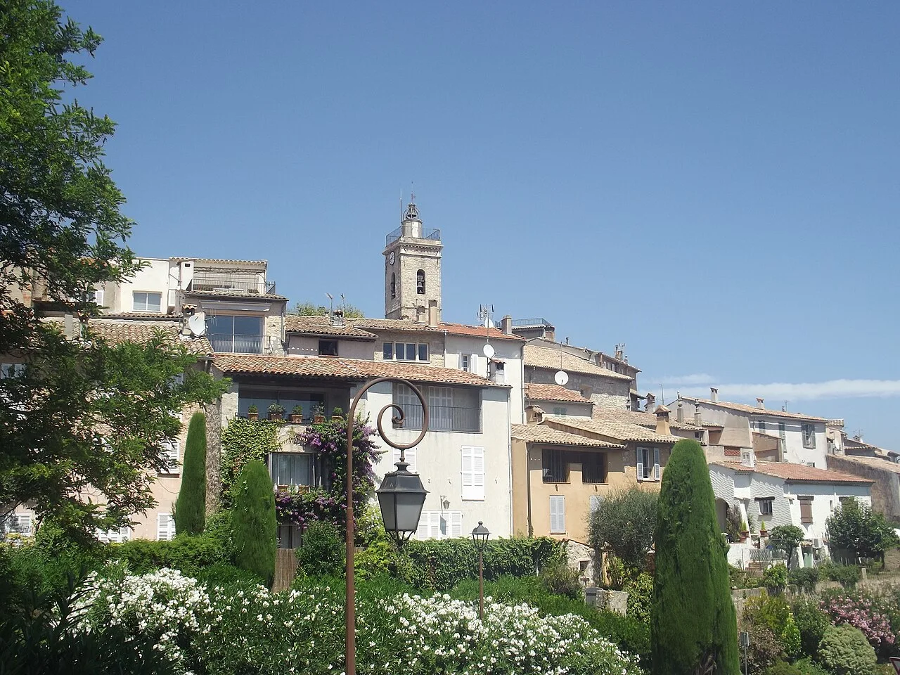 Village perché de Mougins, maisons aux toits de tuiles étagées autour du clocher et végétation au premier plan.